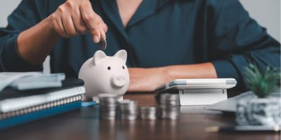 Man sitting learning elbow on desk dropping coin into pic shaped piggy bank.