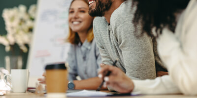 People leaning over table at meeting with coffee